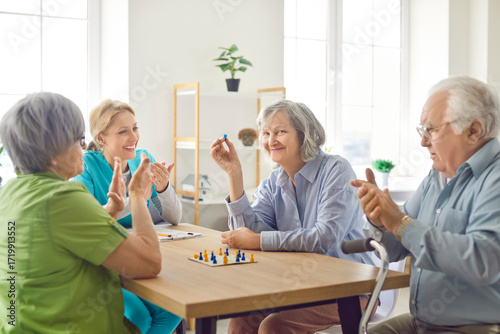 Photos Happy caregiver engaged in entertainment with senior patients, sitting at table and playing board games together at a nursing home