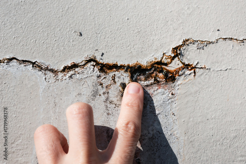 Person inspecting crack in wall with water seeping out. Close up of hand examining  vertical crack in outdoor wall with rust and efflorescence. Repair foundation problems. Selective focus.