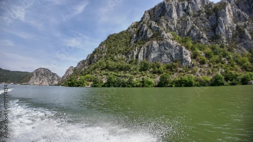 Danube river flowing through the Iron Gates gorge, with steep rocky mountains covered in green vegetation rising from the water, creating a dramatic natural landscape between Serbia and Romania