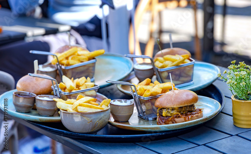 A large platter with three servings of hamburgers, French fries and various sauces is ready to be served to customers.