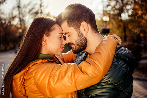 Fotografie Young couple embracing lovingly outdoors during autumn in a sunny park setting,