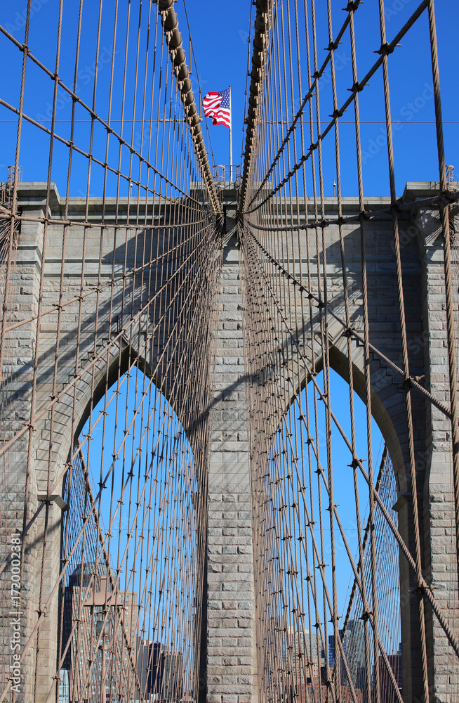 Obraz premium Iconic view of New York city with Waving American Flag on the top of Tower of Brooklyn Bridge and steel cables