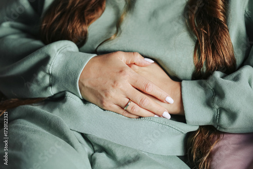 Woman with abdominal pain. Female hands holding stomach. Menstrual cramps symptom closeup. Woman in casual clothes lying. Health care and gynecology issue. Concept of period discomfort.