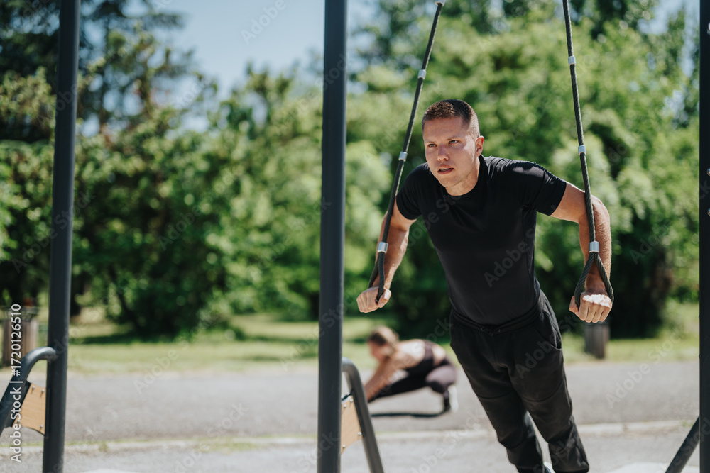 Obraz premium Focused individual performing suspension exercises in an outdoor park setting on a sunny day.