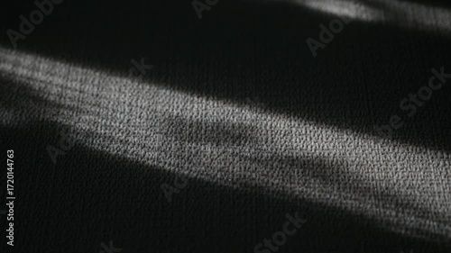 Abstract Light and Shadow on Dark Textile. Close up view of parallel streaks of light illuminating a dark gray textured fabric. 