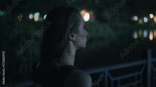 Pensive female silhouetted against glowing urban landscape, soft focus city lights blending with introspective nighttime moment