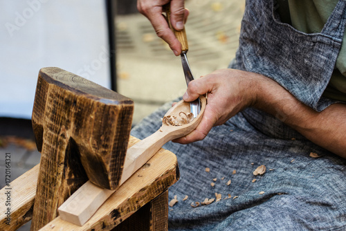 Close-up of a craftsman carving a wooden spoon by hand using traditional woodworking tools. Artisan in apron working with wood, shavings visible. Concept of craftsmanship, handmade