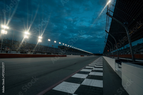 Empty race track at dusk with stadium lights and checkered finish line racing speedway