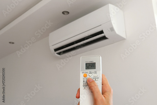 Air conditioner temperature adjustment with remote controller in room at home. Hand holding remote controller of air conditioner inside the white room and set at cool temperature