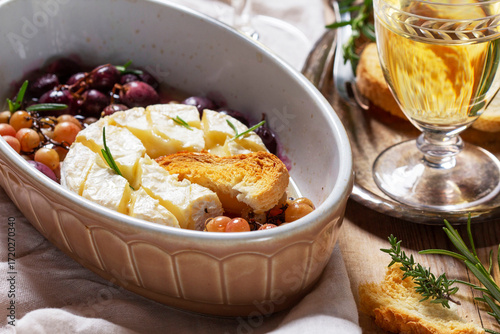 Baked Camembert cheese with grapes, thyme, and rosemary, served with white wine and a baguette.