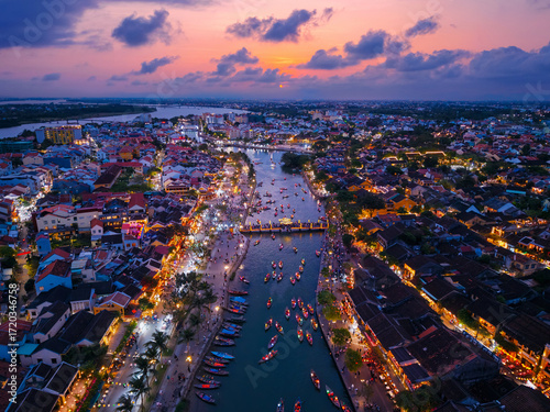 Aerial view of famous landmark bridge of ancient town Hoi An, Vietnam at sunset with lantern-lit boats on thu bon river