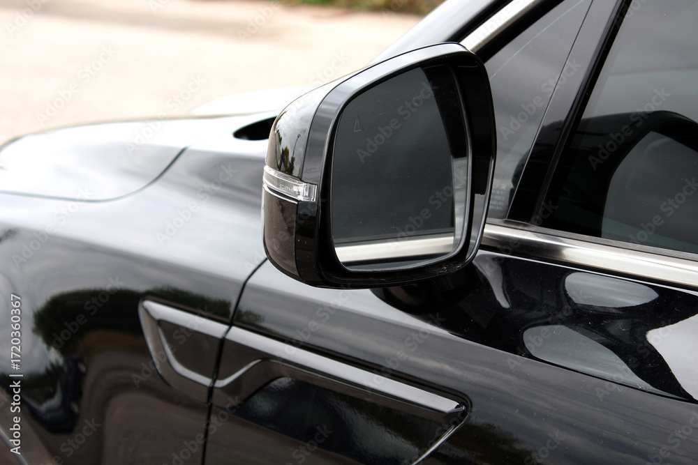 Fototapeta premium Rearview mirror on a black car. Close-up of glossy black car door, featuring a side mirror with chrome trim. Road safety while driving. Black car mirror. Side rear-view mirror lux car.