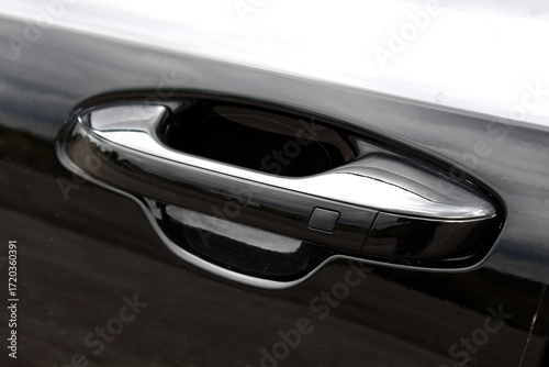 Close-up glossy black car door handle with modern streamlined design, smooth metallic surface, and integrated button. Automatic opening of a car door without a key. Keyless entry car door handle.