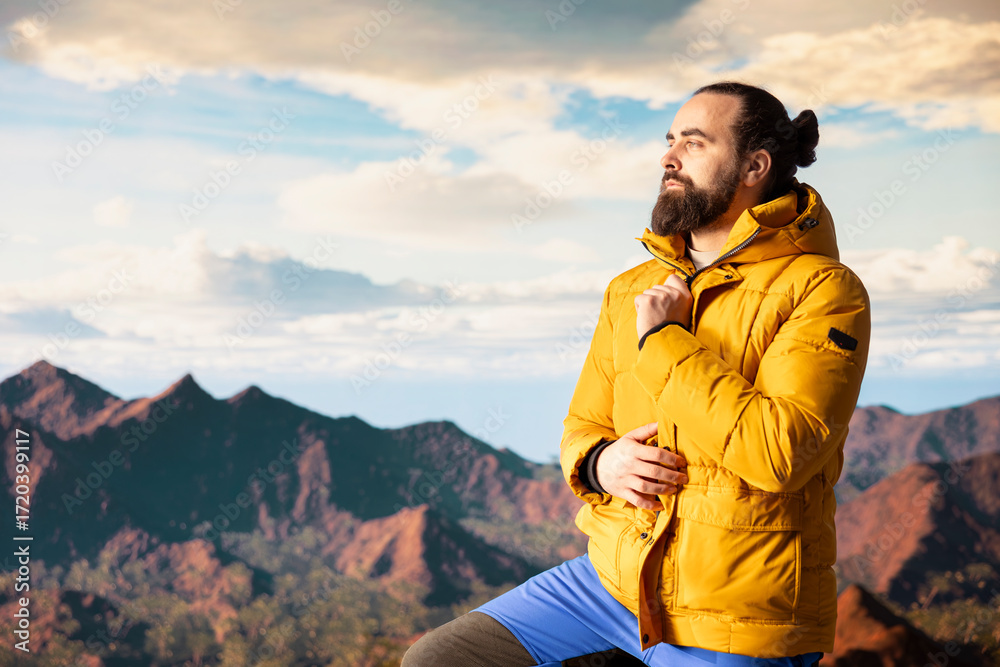 Naklejka premium Male trekker takes in the breathtaking mountain landscape on rocks, enjoying the scenic background, crisp air and rugged peaks. Excitement of discovering new horizons for wellbeing.
