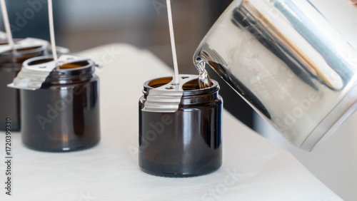 Candle making process pouring melted wax into brown glass jars with wicks
