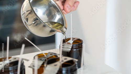 Candle making process pouring melted wax into brown glass jars with wicks