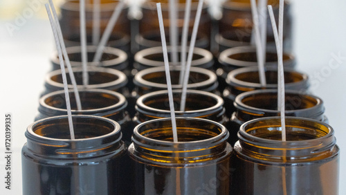 Rows of handcrafted candles with wicks in amber glass jars, ready for pouring.