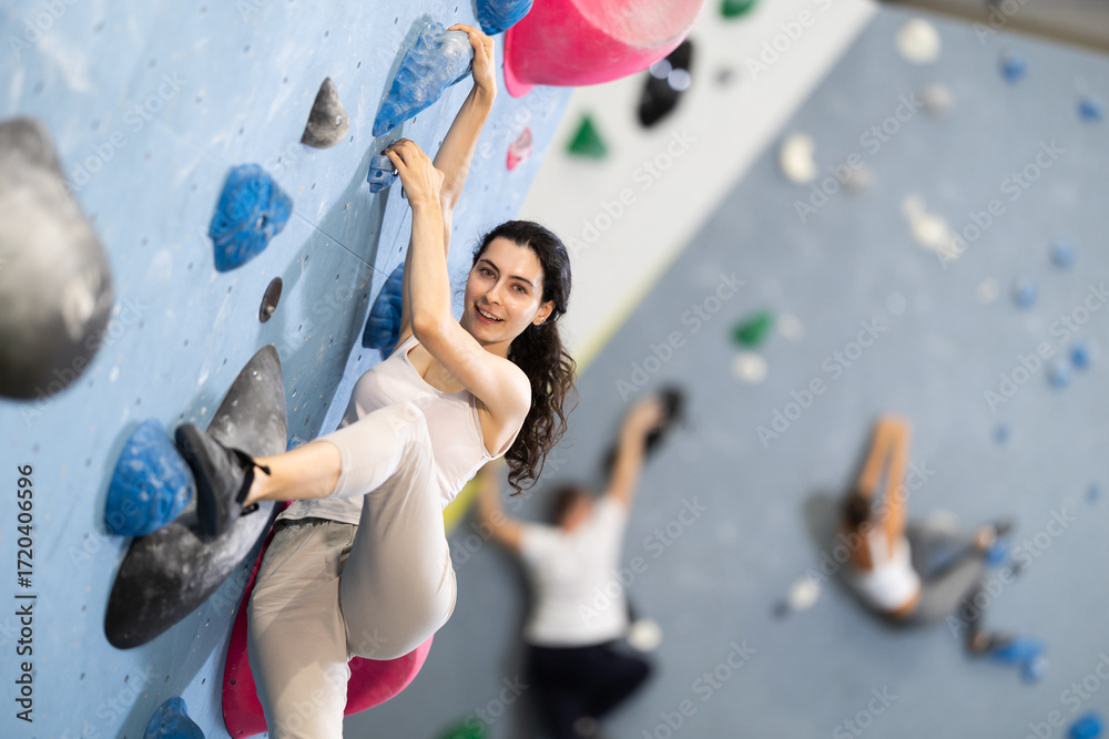 Fototapeta premium Motivated young girl climbing without ropes and harnesses on artificial bouldering wall in modern fitness center