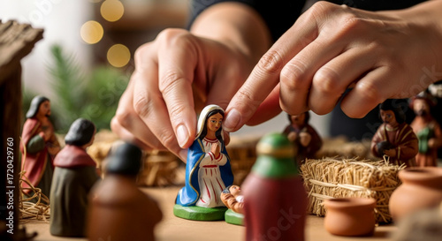 Hands arranging Mary figurine in a nativity scene