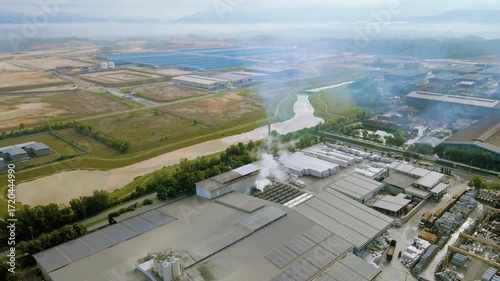 Aerial view of industrial factory with chimney smoke rising, highlighting air pollution and environmental impact in an urban industrial landscape.