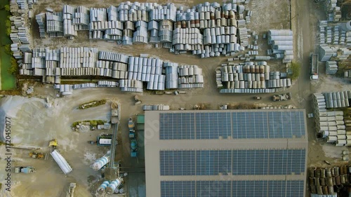 Aerial top view of a cement and concrete factory with rows of pipes, industrial storage, and solar panels on rooftops, showing large-scale construction material production site.