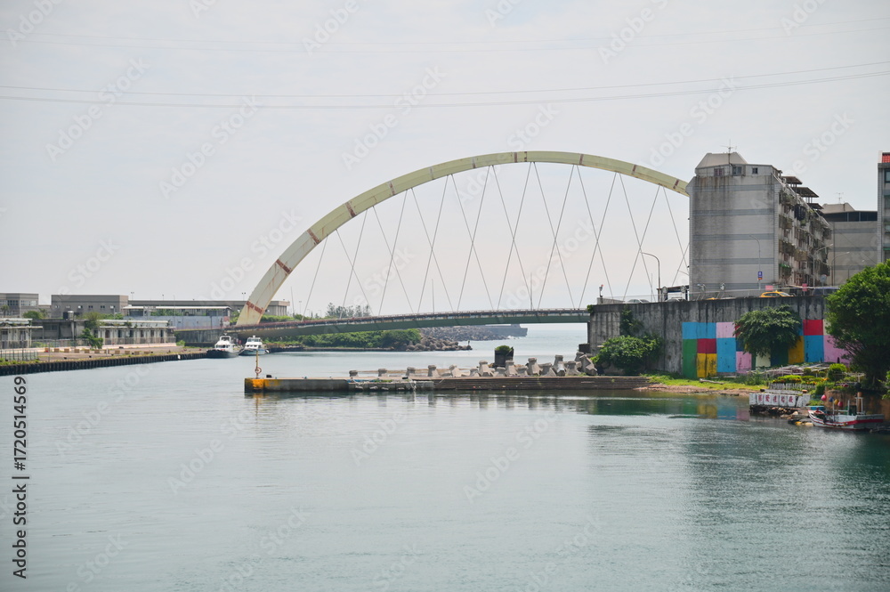 Naklejka premium Taiwan - Jun. 01, 2025: Documentary view of historic Sheliao Bridge spanning harbor waters connecting Keelung mainland to Heping Island with natural lighting and authentic Taiwan coastal architecture.