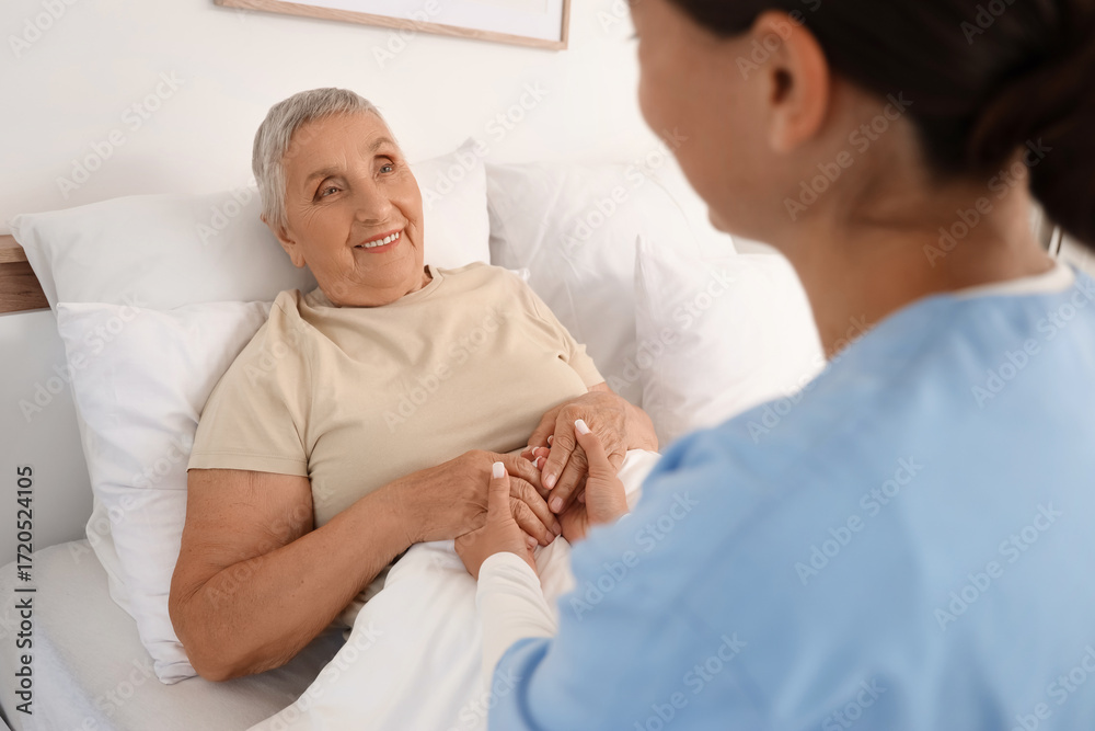 Fototapeta premium Female caregiver with happy senior woman holding hands in bedroom