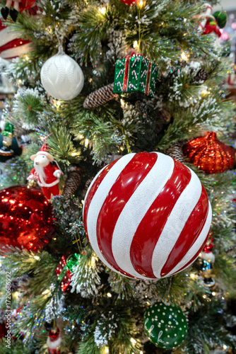 Close-up of a large red and white striped Christmas ornament ball. Festively decorated Christmas tree. Vertical photo