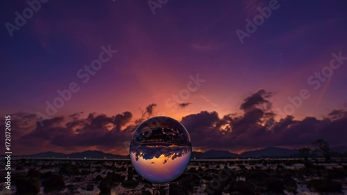 Time lapse A mesmerizing sunset over a rocky shoreline captured through a glass crystal ball, creating a surreal inverted reflection of the seascape beneath vibrant, colorful skies.