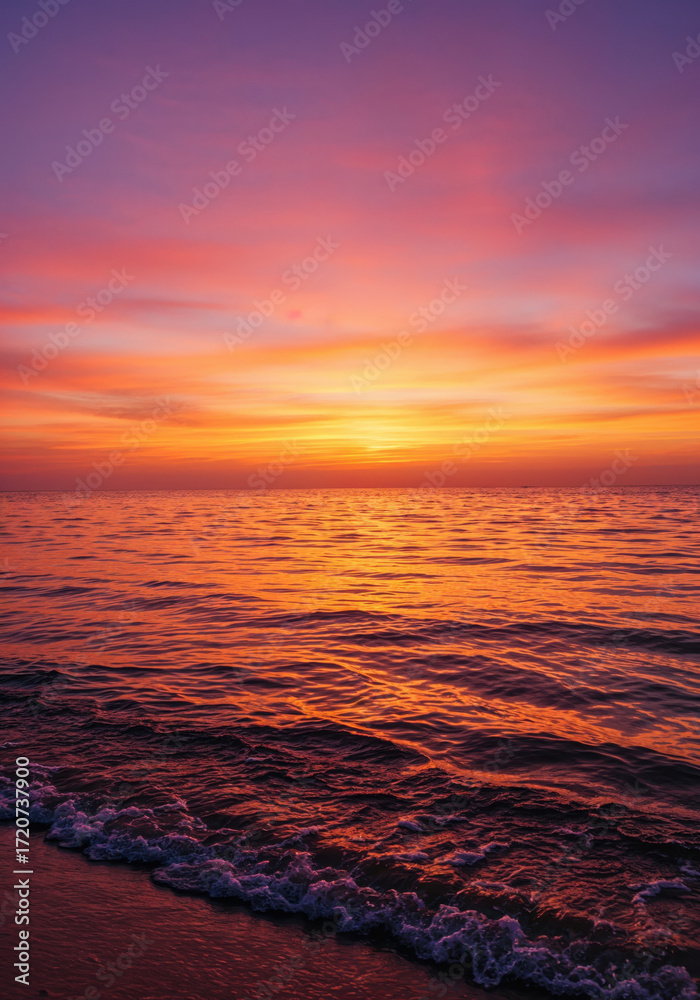 Fototapeta premium Vibrant Sunset Over the Ocean: A breathtaking scene unfolds as the sun dips below the horizon, painting the ocean and sky with a radiant symphony of colors. The calm water reflects the vivid hues.