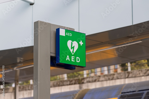 Green AED sign at a modern train station in the Netherlands. Public defibrillator symbol for emergency heart resuscitation access.