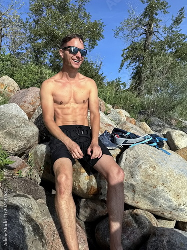 Happy mature handsome shirtless man sitting on a rock