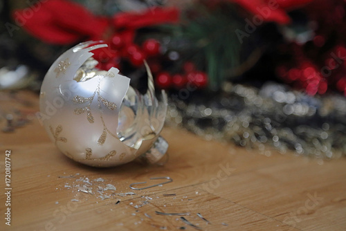 The shards and remnants of a broken Christmas bell ornament are shown on the floor next to colorful holiday tree decorations.