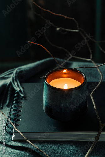 Burning candle in ceramic holder on notebook with cozy atmosphere, soft light, autumn mood and warm rustic still life.