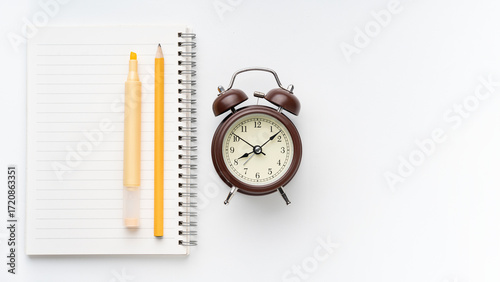Vintage alarm clock with notebook, highlighter, and pencil, perfect for time management, study, or creative project concepts on a clean white surface