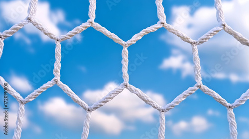 Close up of a soccer goal net against blue sky and fluffy clouds  