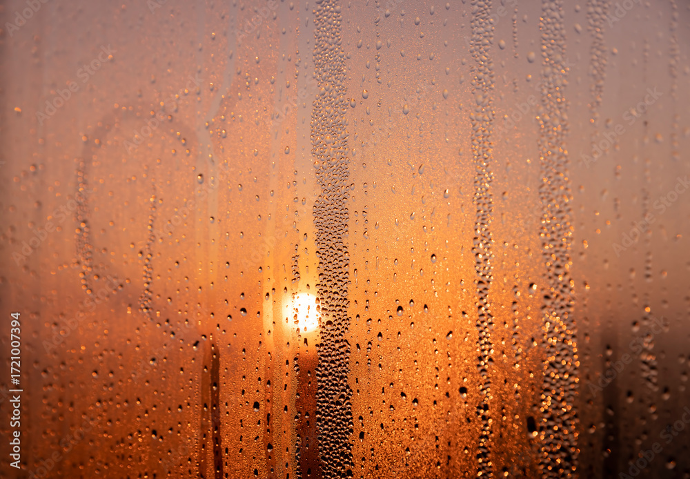 Fototapeta premium water droplets from condensation on the window glass at sunset, wet glass with lots of water droplets on the background of an orange sky out of focus at sunset