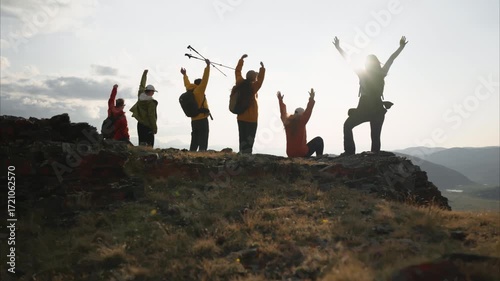 Wide angle bottom view of a group of diverse hikers man and woman celebrating reaching the summit in the Altai Mountains. Trekkers raise their hands in the background of sunset sky