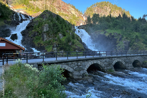 Landscape photo with a view of the cascades of the Latefossen waterfall, a stone arch bridge and mountains in the background at sunset near Skare in Norway