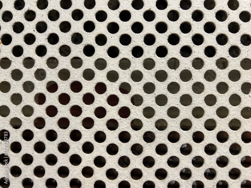 Close-up of perforated metal surface with symmetrical circular holes and shadow variations – ideal industrial texture for engineering, ventilation systems, or design backgrounds.