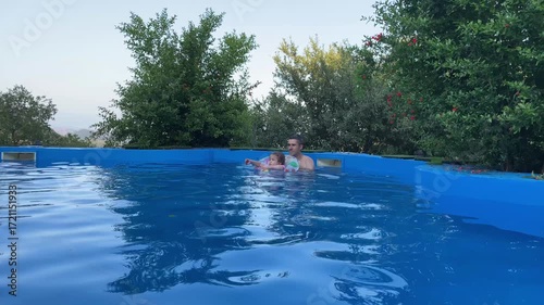 Family Dad and Daughter Swimming in Pool on Sunny Day in Summer with Inflatable Ring
