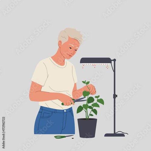Person trims potted plant with grow light on soft grey background