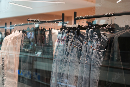 a clothing rack in a store displaying denim jeans, shirts, and jackets neatly hung on black hangers