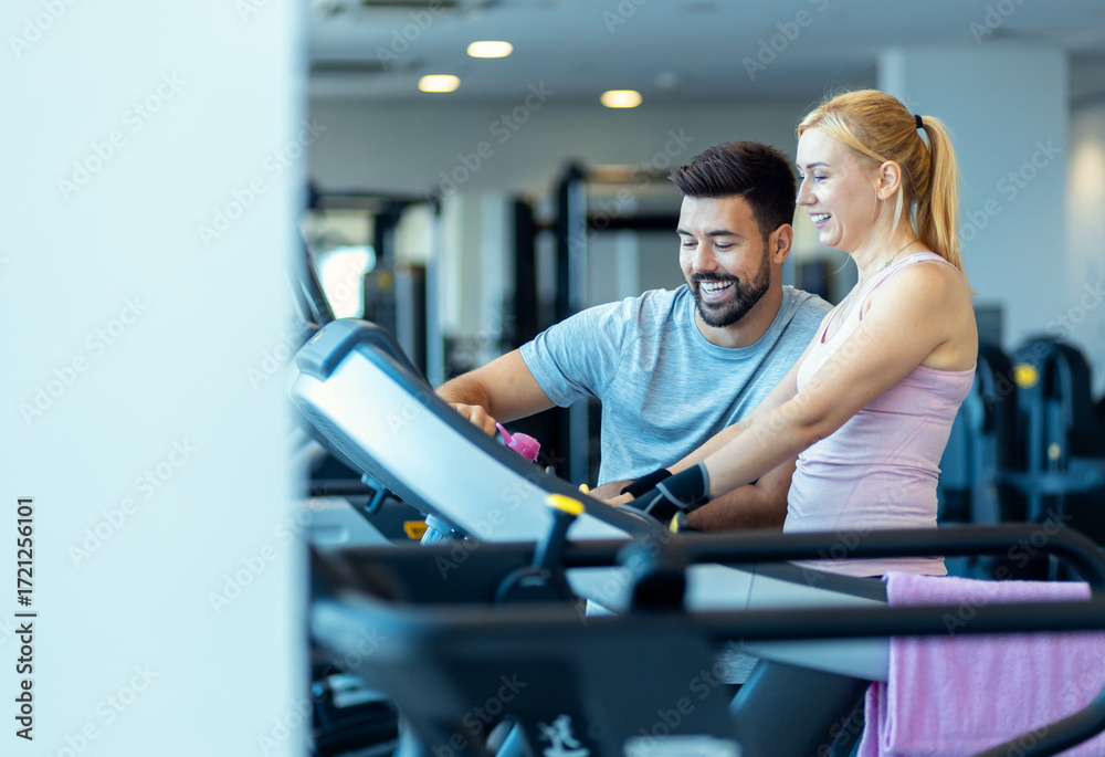 Obraz premium Mid adult woman and personal fitness trainer preparing for workout on treadmill at gym.