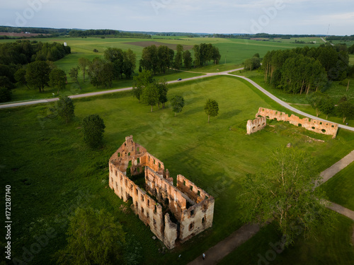 Aerial view of the weathered ruins standing silently amidst the vibrant green fields, a stark contrast against the clear sky, Merkine, alininkai, Lithuania.