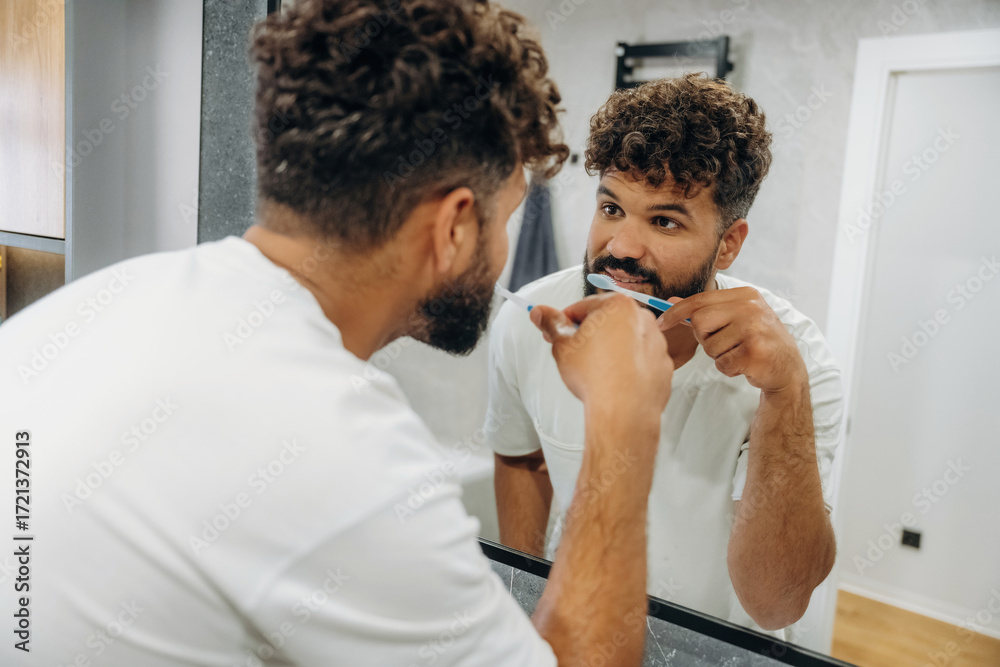 Fototapeta premium Brushing the teeth. Guy is in the bathroom, taking care of his appearance
