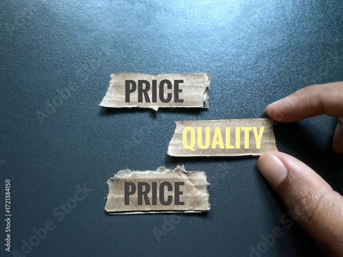 A hand choosing cardboard piece labeled with Quality word. Word Price also written on cardboard pieces.