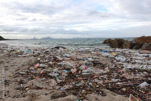 Trash on the beach, the shoreline is heavily littered with plastic bottles, food containers, and other marine debris. The polluted coast highlights the problem of ocean pollution.