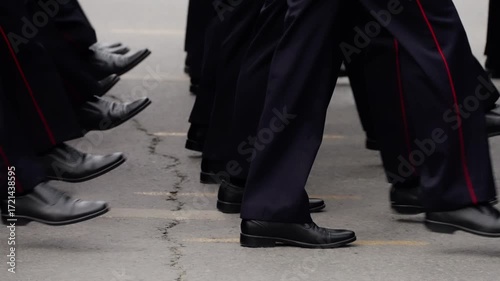 Close-up view of uniformed personnel marching in synchronized formation, polished black shoes and navy trousers stepping in cadence along a roadway during a disciplined drill