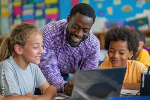 Male teacher helping elementary students with a laptop in the classroom